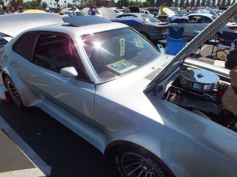 2003 Ford Crown Victoria - custom silver coupe sits with its hood open exposing a chromed Cobra-valve-cover V8, set off by wide flares and a red interior.