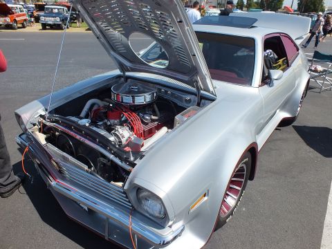 2003 Ford Crown Victoria - silver custom hatchback displays a polished V8 with red accents under its open hood, fender flares and red-lettered tires at a car show.