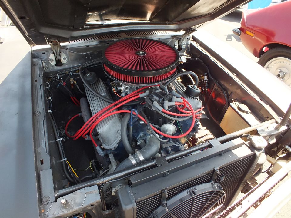 Engine bay with red round air filter, blue V8, red plug wires and electric fan