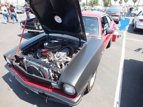 2003 Ford Crown Victoria - maroon coupe with a flat-gray hood propped open reveals a V8 and front-mounted electric fan in a parking-lot car show.