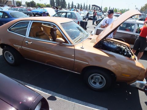 2003 Ford Crown Victoria - copper-brown Ford Pinto hatchback shown in profile has its hood up, a tan interior and chrome mag wheels at a car show.
