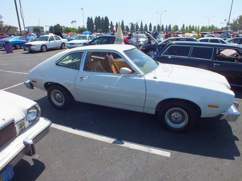 2003 Ford Crown Victoria - white Ford Pinto hatchback is shown in clean profile with a tan interior and wire-style wheel covers at a sunny car show.