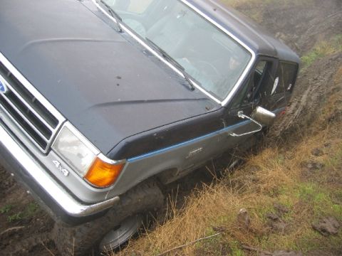 1989 Ford Bronco - A Ford Bronco navigates a muddy terrain, its tires sinking into the wet ground.