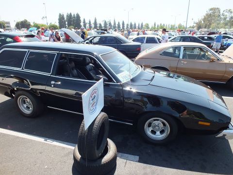 2003 Ford Crown Victoria - black vintage two-door station wagon parked at a sunny outdoor car show, with a club display sign propped on stacked tires.