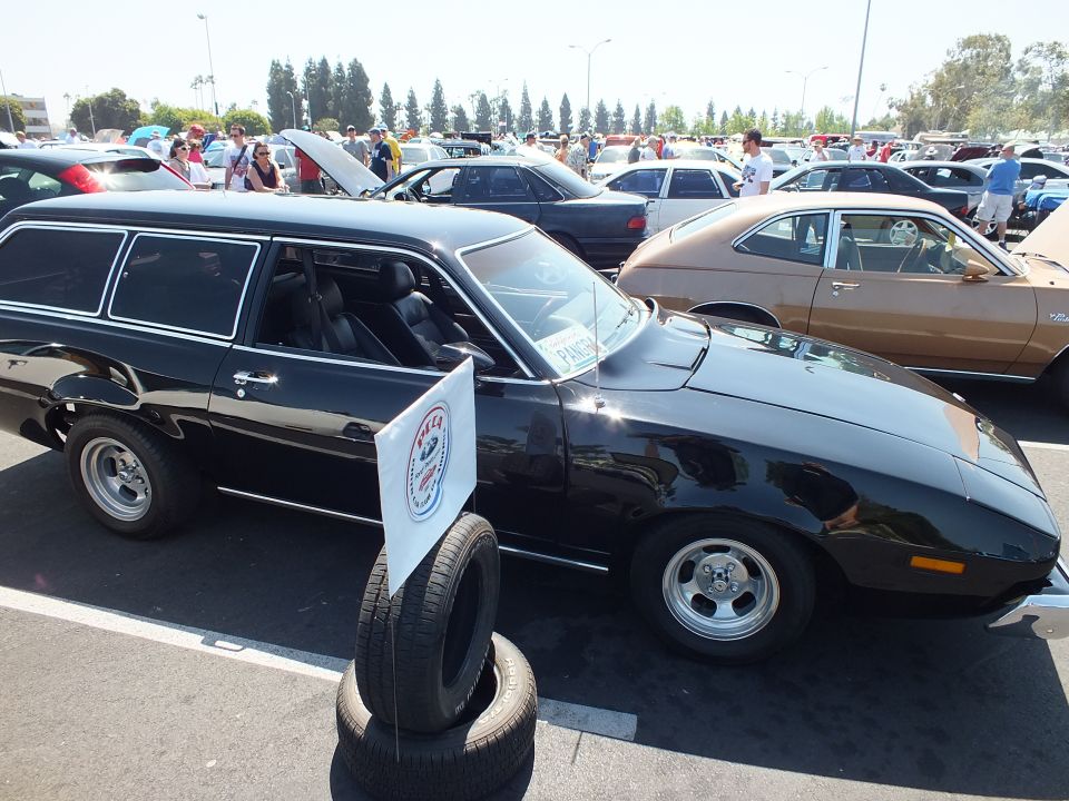 Black two-door station wagon at outdoor car show, club sign on tires in foreground