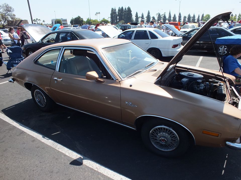 Brown two-door hatchback with wire wheels and open hood at car show