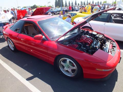 2003 Ford Crown Victoria - red sports coupe with a sunroof and raised hood, parked among a crowd of spectators at a car show.