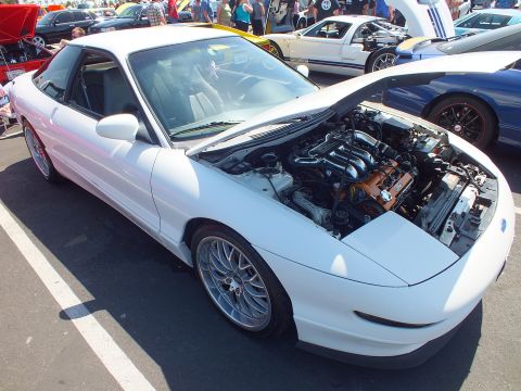 2003 Ford Crown Victoria - white sports coupe with multi-spoke wheels and its hood raised exposing the engine bay at a car show.