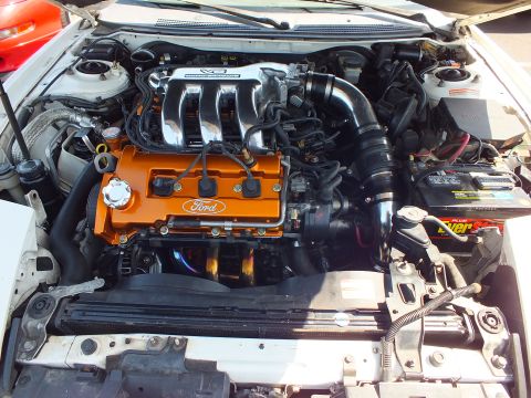 2003 Ford Crown Victoria - Close-up of an engine bay featuring an orange-painted valve cover marked Ford alongside a black battery.