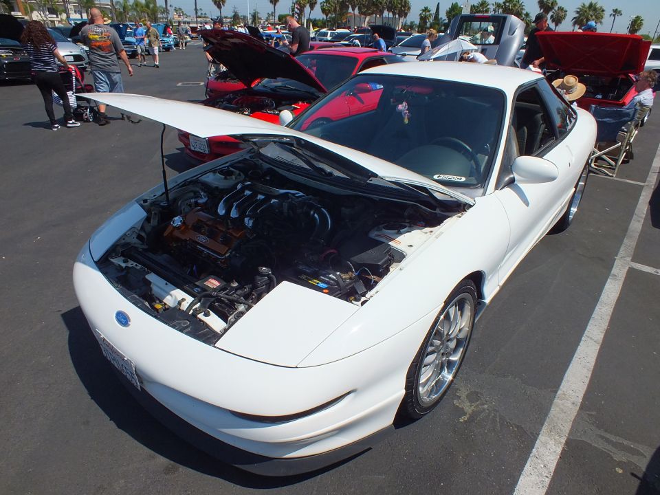 White coupe with sunroof and open hood, top-down front view at car show