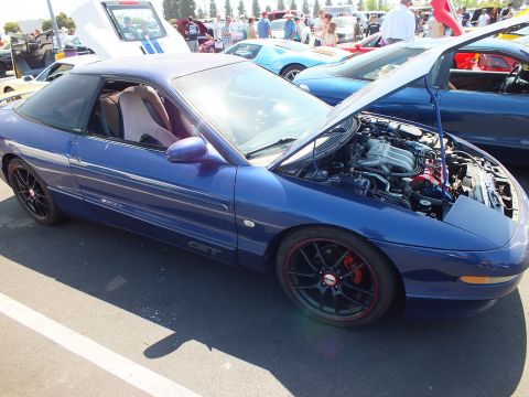 2003 Ford Crown Victoria - dark blue sports coupe with black multi-spoke wheels and red brake calipers, hood raised at a car show.