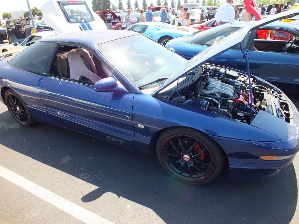 Dark blue coupe with black wheels and open hood at car show