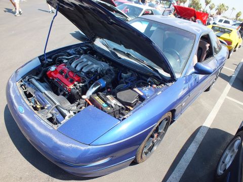 2003 Ford Crown Victoria - blue sports coupe with gold-finished wheels and its hood raised exposing the engine bay at a car show.