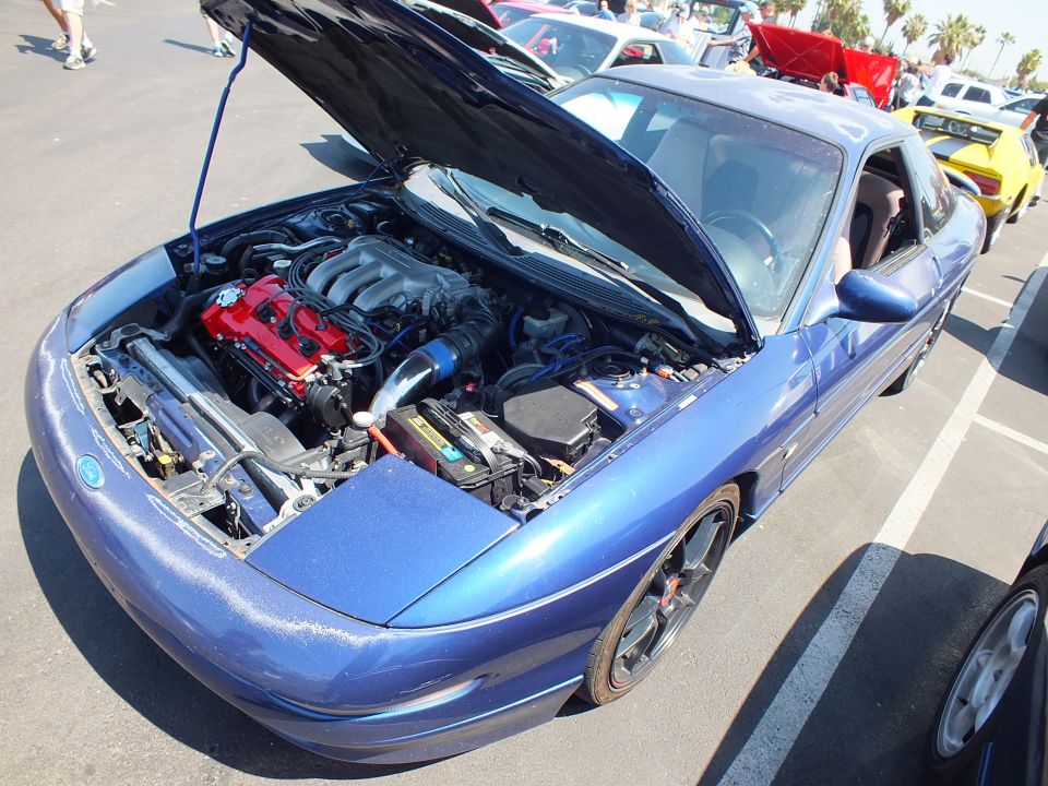 Blue coupe with hood up showing engine, gold wheels at car show