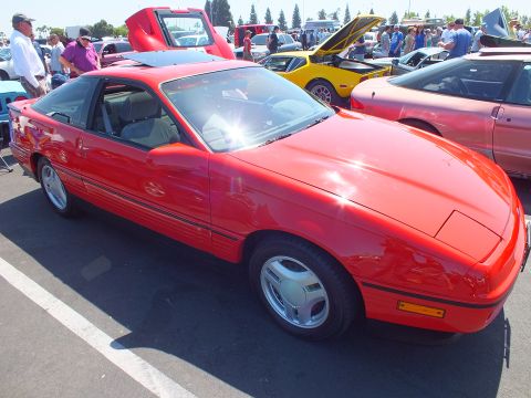 2003 Ford Crown Victoria - red 1980s hatchback coupe shown in profile with chrome multi-spoke wheels at an outdoor car show.