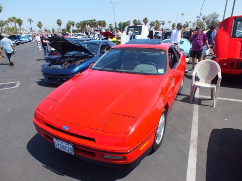 2003 Ford Crown Victoria - red 1980s coupe with pop-up headlights shown front-on, displaying a California license plate at a car show.
