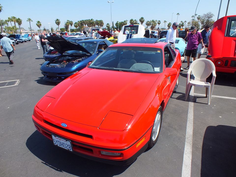 Red coupe with pop-up headlights, front view, California plate at car show