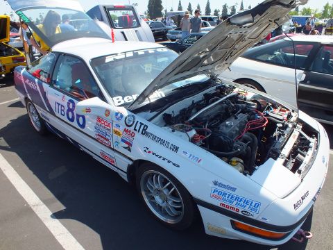 2003 Ford Crown Victoria - white sports coupe in race livery with sponsor decals and the number 80 has its hood open at a car show.