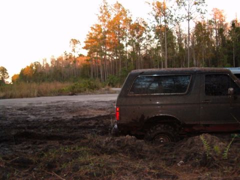 1991 Ford Bronco - Ford Bronco stuck in mud with trees in the background.