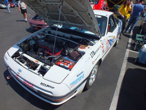 2003 Ford Crown Victoria - white sports coupe covered in sponsor decals sits with its hood open among other cars at an outdoor show.