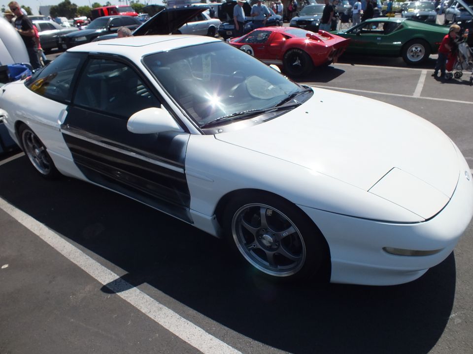 White two-tone sports coupe with dark side panel and chrome wheels parked at a car show