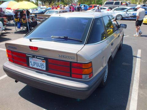 2003 Ford Crown Victoria - rear of a tan Merkur hatchback shows its badge and California plate while parked at an outdoor car show.