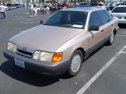 2003 Ford Crown Victoria - tan 1980s Ford four-door sedan with a Ford emblem is parked front-three-quarter among show cars and spectators.