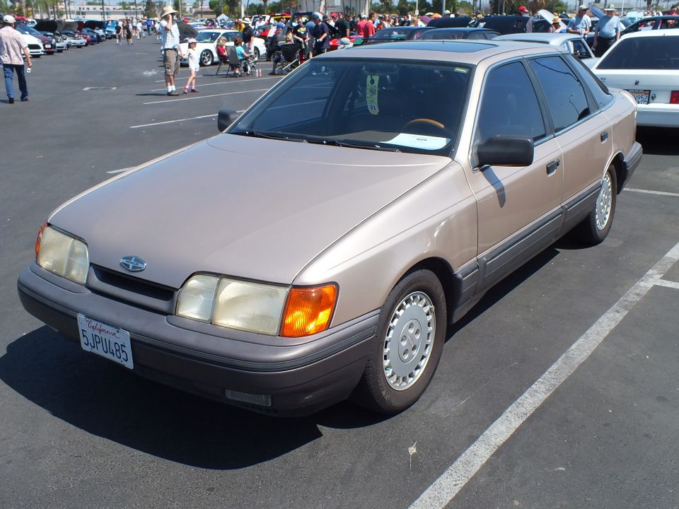 Tan Ford four-door sedan from the 1980s parked front-three-quarter at a car show