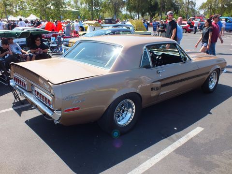 2003 Ford Crown Victoria - gold-bronze classic Ford Mustang coupe with a GT/CS badge and chrome wheels sits rear-three-quarter at a show.