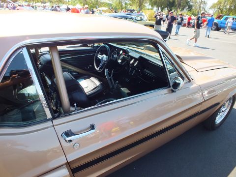2003 Ford Crown Victoria - Looking through the side window of a gold classic Mustang reveals a roll cage and a wood-rimmed steering wheel.