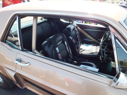 2003 Ford Crown Victoria - Through the side window of a tan classic Mustang are black bucket seats with harnesses and a roll cage.