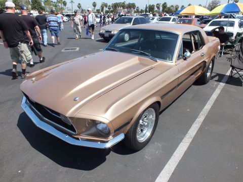 2003 Ford Crown Victoria - gold-bronze classic Mustang coupe with chrome bumper sits front-three-quarter amid crowds at an outdoor show.
