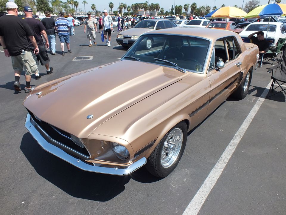 Gold-bronze classic Mustang coupe front-three-quarter among show cars and crowds