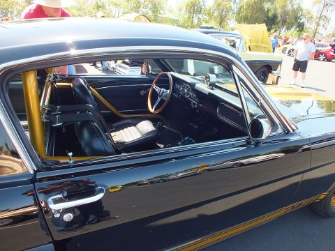 2003 Ford Crown Victoria - Through the side window of a black classic Mustang are a gold roll cage, wood-rim wheel and white-insert seats.