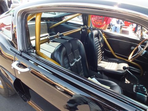 2003 Ford Crown Victoria - Interior detail of a black classic Mustang shows a gold roll cage, bucket seats with harnesses and a fire extinguisher.
