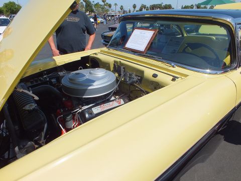 2003 Ford Crown Victoria - engine bay of a pale yellow classic car shows a large round chrome air cleaner and a placard, viewed under the raised hood.