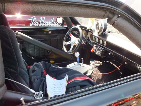 2003 Ford Crown Victoria - stripped interior of a race car shows a roll cage, racing steering wheel, shifter and a Talladega badge on the dash.