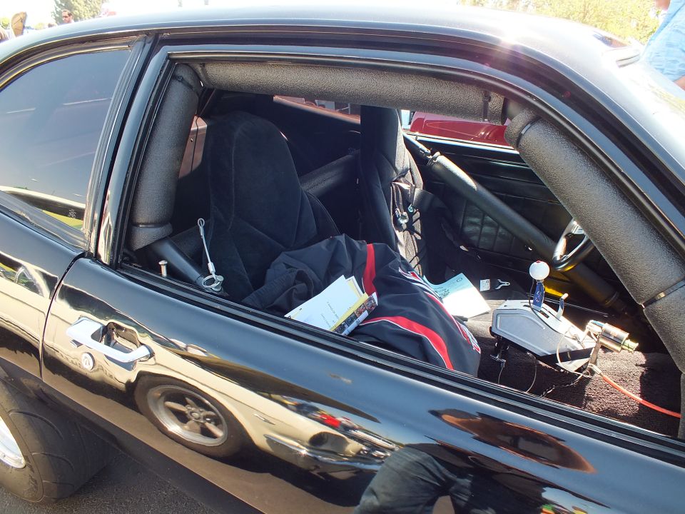 Interior of black car through open window showing racing seat and roll cage