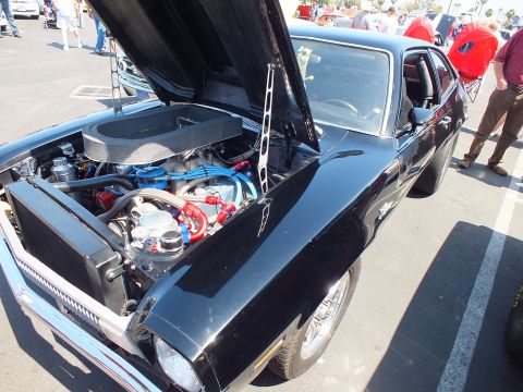 2003 Ford Crown Victoria - glossy black coupe sits with hood raised, exposing a detailed engine with blue wires, beside chrome wheels at an outdoor show.