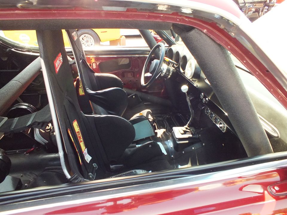 Interior of red race car with black racing seat, roll cage and steering wheel
