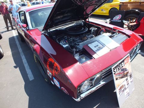 2003 Ford Crown Victoria - maroon vintage fastback with race decals sits with hood raised beside a Street Cup poster in a sunny show parking lot.