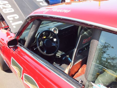 2003 Ford Crown Victoria - View through the side window of a red race car revealing a roll cage, racing steering wheel and a single mounted gauge.