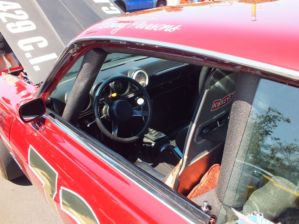 Interior of red race car showing roll cage, steering wheel and single gauge through window