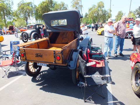 2003 Ford Crown Victoria - rear of an antique Ford pickup with a wooden bed and embossed tailgate, surrounded by folding chairs at an outdoor show.