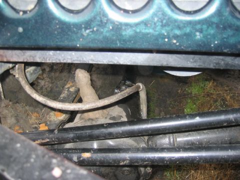 1989 Ford Bronco - Close-up view of the undercarriage of a vehicle, showing mechanical parts and the ground below.