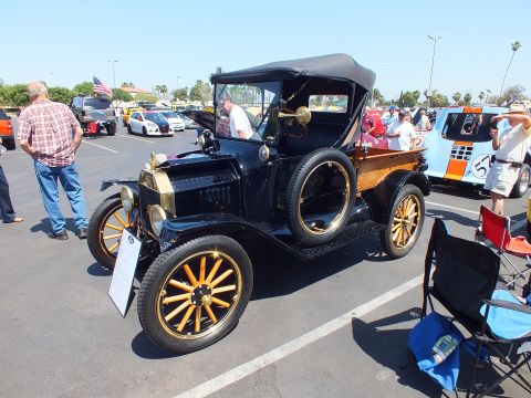 2003 Ford Crown Victoria - black antique Ford open car with brass trim, folding canvas top and yellow wooden-spoke wheels parked at an outdoor show.