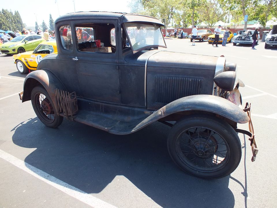 Weathered black antique coupe with patina, side view on spoke wheels at car show