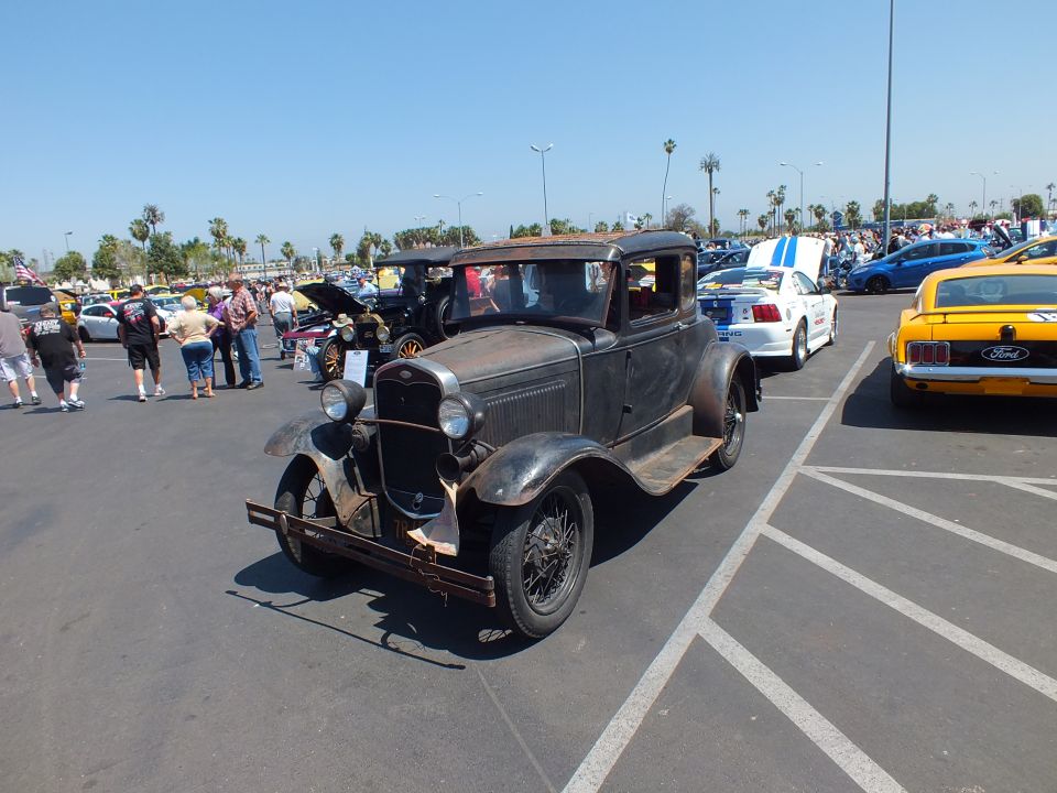 Weathered antique black Ford coupe with patina parked in lot, front quarter view