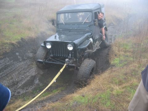 1989 Ford Bronco - A dark green jeep is stuck in a muddy ditch, with a yellow strap attached to its front bumper.