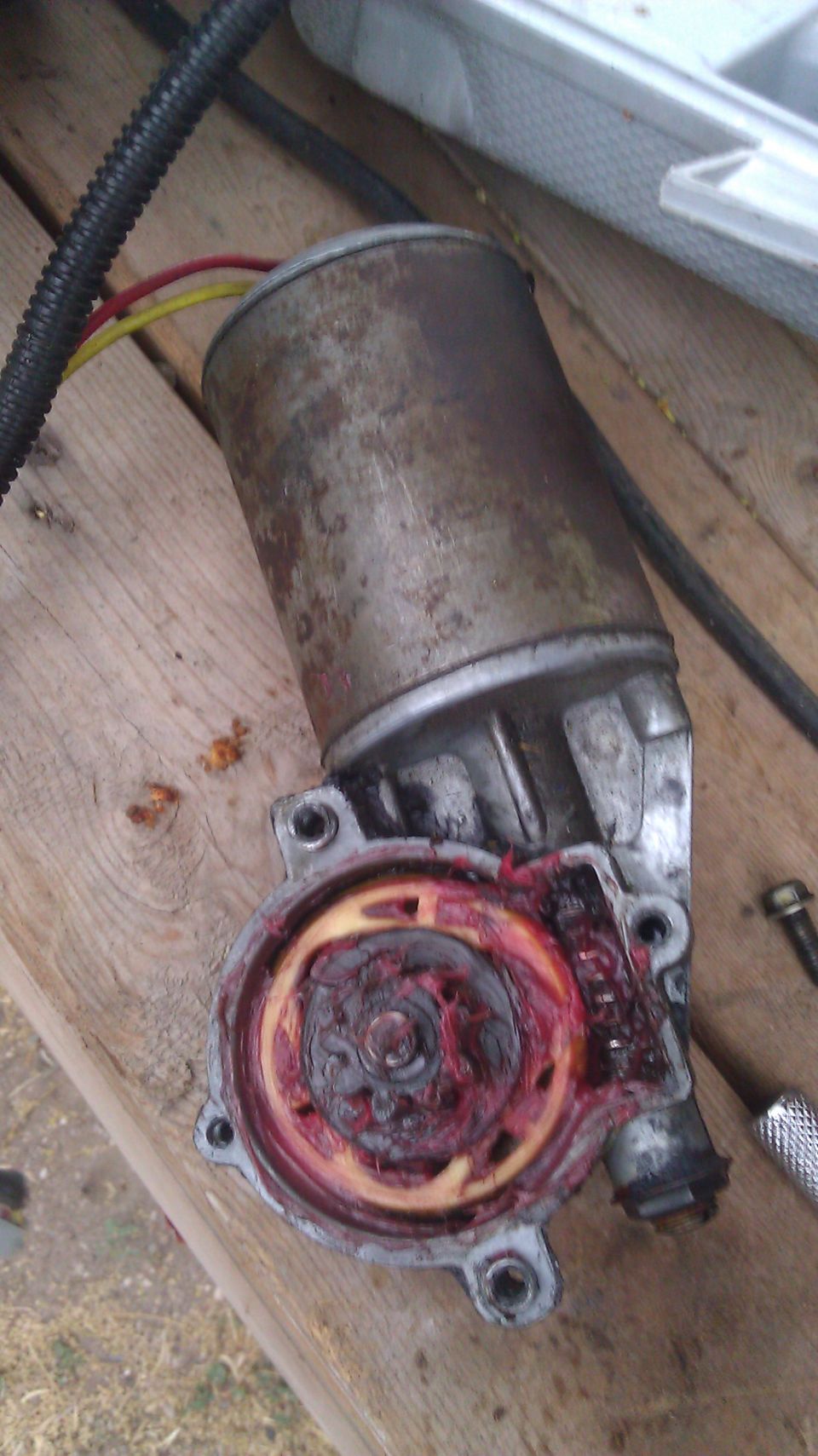 Disassembled electric shift motor showing gear covered in red grease, sitting on wooden boards